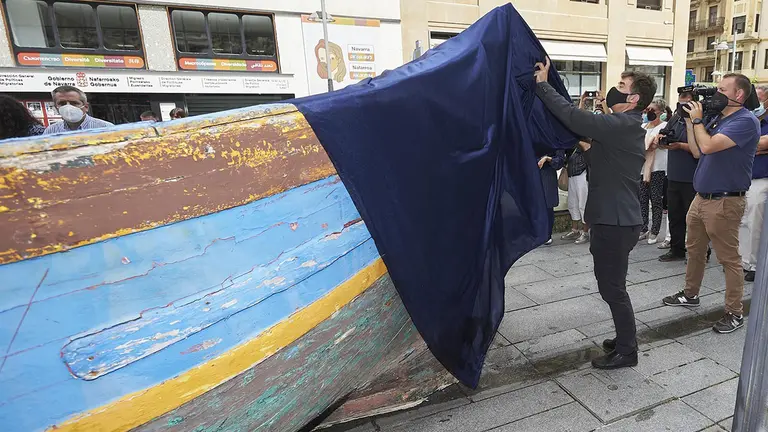 El consejero Santos retira la lona que cubre una patera, protagonista de la exposición para conmemorar el Día Mundial de las Personas Refugiadas. GOBIERNO DE NAVARRA