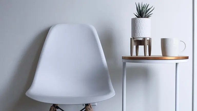 Una mesilla con una planta y una taza junto a una silla. ARCHIVO