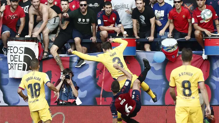 El defensa del FC Barcelona Gerard Piqué (c. arriba) comete penalti sobre Oier Sanjurjo, de Osasuna, en el partido correspondiente a la 3ª Jornada de LaLiga Santander que Osasuna y FC Barcelona disputan hoy sábado en el estadio El Sadar, en Pamplona. EFE/Jesús Diges