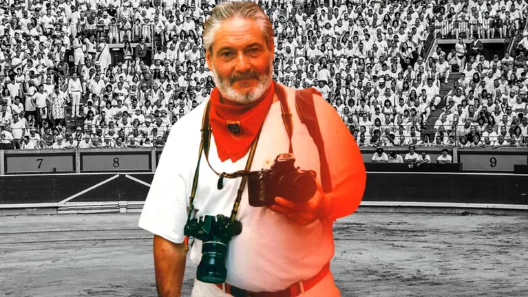 José Luis Nobel sobre un fondo de la plaza de toros de Pamplona y con atuendo sanferminero con sus inseparables cámaras.