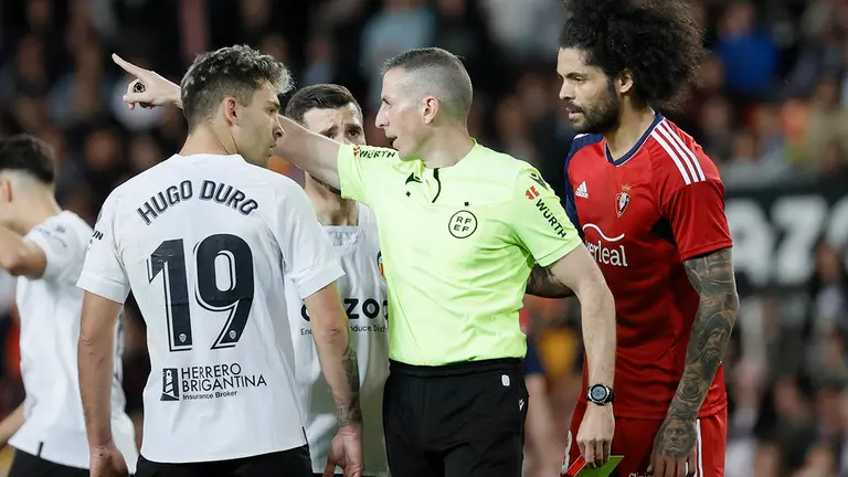 El colegiado Iglesias Villanueva tras mostrar tarjeta amarilla al delantero del Valencia, Hugo Duro (i), durante el partido correspondiente a la jornada 25 de primera división que disputan hoy sábado Valencia y Osasuna en el estadio Mestalla de Valencia. EFE/ Juan Carlos Cárdenas