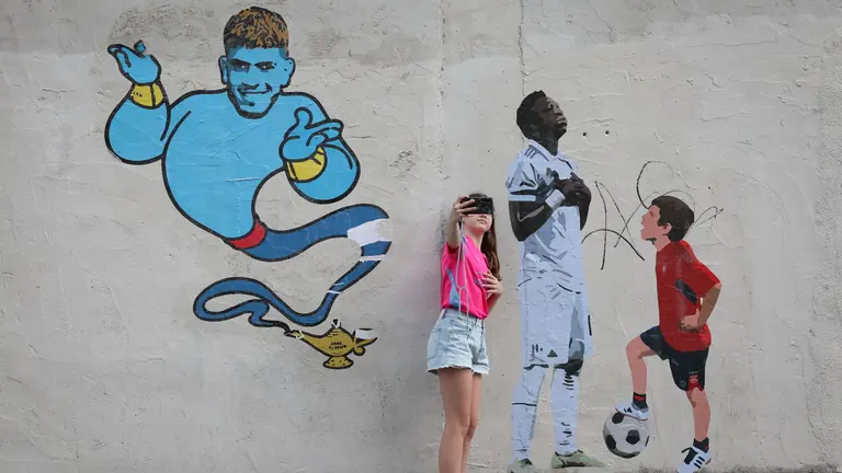 Un par de niños se fotografía este sábado junto a un mural del artista LKN en la que un joven rojillodesafía a Vinícius Júnior, estrella del Real Madrid. La final de Copa que disputa este sábado el CA Osasuna contra el Real Madrid flota en el ambiente de cualquier rincón de Navarra y los tintes osasunistas toman fuerza en Pamplona. EFE/Villar López