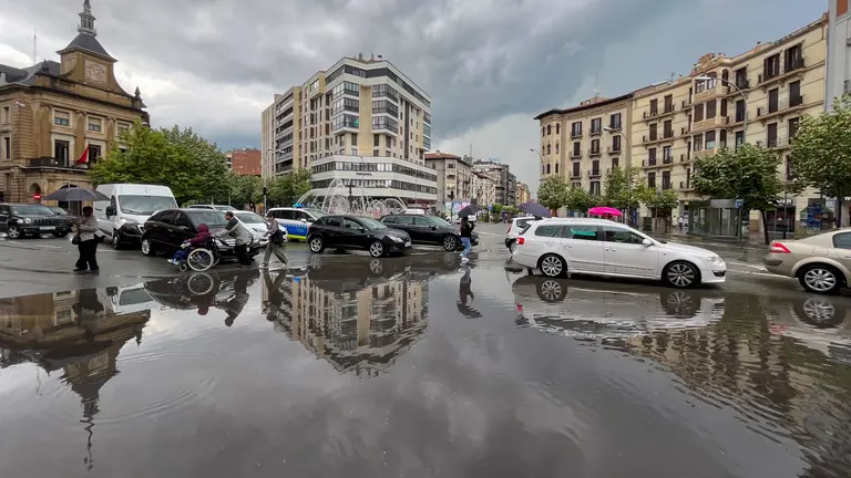 Varias personas cruzan por mitad de la Plaza de las Merindades de Pamplona donde fuerte tormenta ha descargado en media hora, más de 16 litros y ha dificultado el tráfico en distintos puntos de la comarca. EFE/Villar López