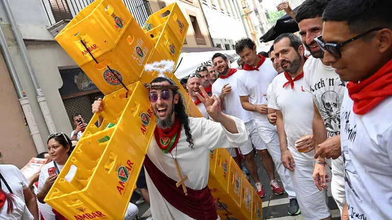 Un joven desfila con una cruz de cajas de cervezas. Miles de personas se han dado cita en el casco antiguo de Pamplona para presenciar el recorrido de la imagen de San Fermín que ha salido este viernes en procesión ,acompañado por el cabildo catedralicio, la Corporación, la banda de música La Pamplonesa y la Comparsa de Gigantes y Cabezudos. EFE/ Eloy Alonso
