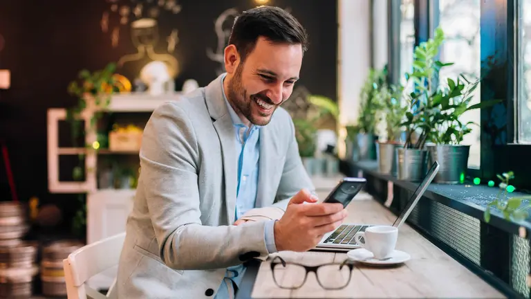 Una persona trabaja con un ordenador portatil y su teléfono móvil mientras toma un café