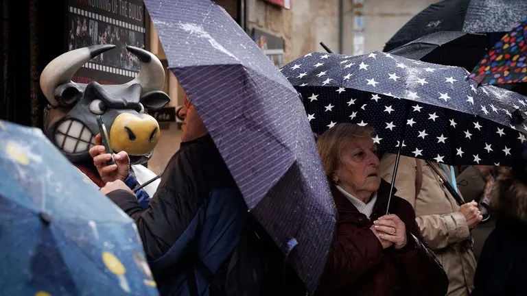 Varias personas se protegen de una intensa lluvia este viernes en la calle de La Estafeta de Pamplona en una jornada en la que la vertiente cantábrica de Navarra y el Pirineo se encuentran en aviso amarillo por precipitaciones y acumulación de nieve, una situación que pondría en riesgo la procesión de Viernes Santo de la capital nvarra así como otros actos de Semana Santa a lo largo y ancho de la comunidad Foral. EFE/ Villar López