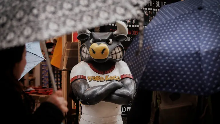 Varias personas se protegen de una intensa lluvia este viernes en la calle de La estafeta de Pamplona en una jornada en la que la vertiente cantábrica de Navarra y el Pirineo se encuentran en aviso amarillo por precipitaciones y acumulación de nieve, una situación que pondría en riesgo la procesión de Viernes Santo de Pamplona así como otros actos de Semana Santa a lo largo y ancho de la comunidad Foral. EFE/ Villar López