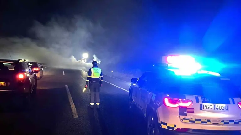 Un agente de la Guardia Civil regula el tráfico junto al coche humeante en la Autopista de Navarra. GUARDIA CIVIL