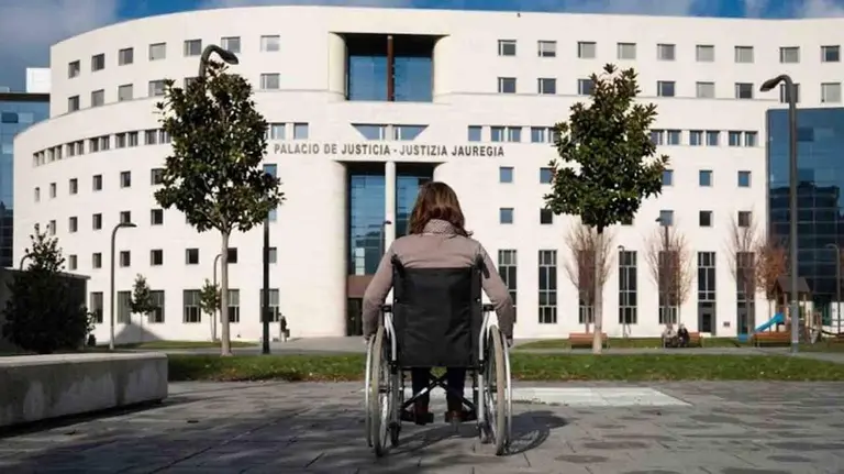 Una mujer en silla de ruedas frente al edificio de la Audiencia de Pamplona.