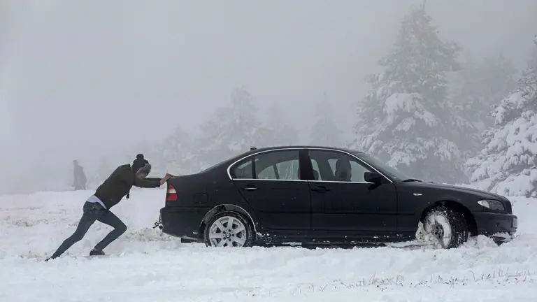 Una persona empuja un coche que ha quedado atrapado en la nieve. EFE/Villar López
