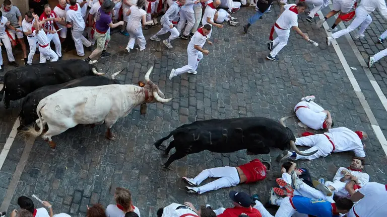 Varios mozos esquivan a los toros de la ganadería gaditana de Fuente Ymbro en el tramo desde el final de la cuesta de Santo Domingo a la curva de Mercaderes durante el segundo encierro de los Sanfermines 2022. EFE/J.P. Urdiroz