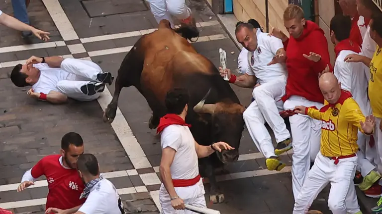 Un mozo es volteado por un toro de la ganadería de Fuente Ymbro al inicio de la calle de la Estafeta durante el cuarto encierro de los sanfermines 2023, este lunes. EFE -J.P. Urdiroz