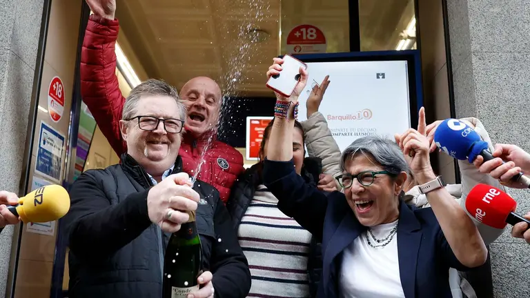 Varias personas celebran a las puertas de la administración de loterías del número 10 de la calle Barquillo, en Madrid, donde se ha vendido íntegramente el 70.048, el segundo premio del Sorteo Extraordinario de la Lotería de Navidad. EFE/Mariscal
