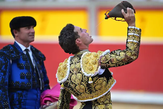 El torero Fernando Adrián bebe de una bota de vino durante la vuelta al ruedo tras cortar una oreja a su segundo toro de la tarde en la octava de abono de la Feria del Toro de los Sanfermines 2026 con toros de la ganadería gaditana de La Palmosilla y en la que ha compartido cartel con los diestros Jiménez Fortes y Samuel Navalón. EFE/ Daniel Fernández.