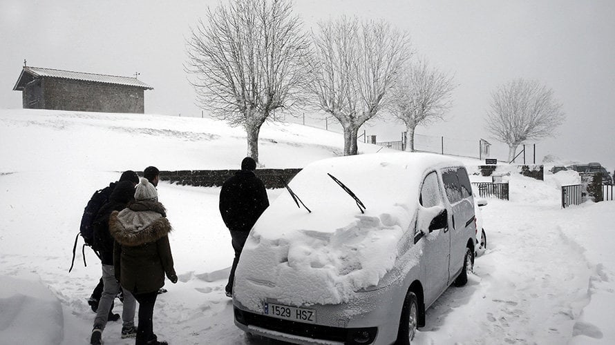 Un grupo de personas pasa ante un vehículo cubierto de nieve aparcado junto al Santuario de San Miguel de Aralar, en una jornada de nieve de 2016. EFE/Jesús Diges