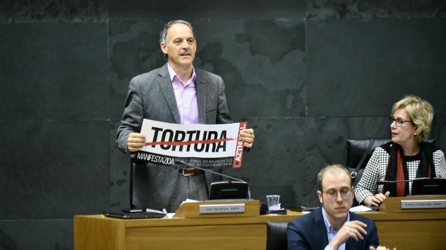 Adolfo Araiz, portavoz de Bildu, ha permanecido de pie, retando al resto de la Cámara con su cartel. PABLO LASAOSA.