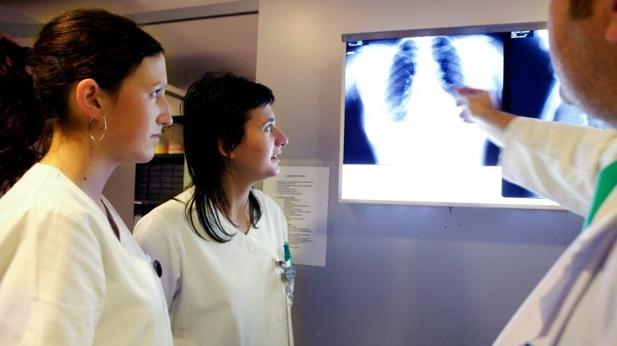 Dos estudiantes de Enfermería se muestran atentas ante las explicaciones de un médico.
