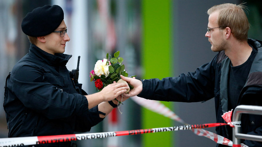 Un hombre entrega unas flores a un policía junto a la zona de Múnich donde ocurrió el tiroteo. REUTERS