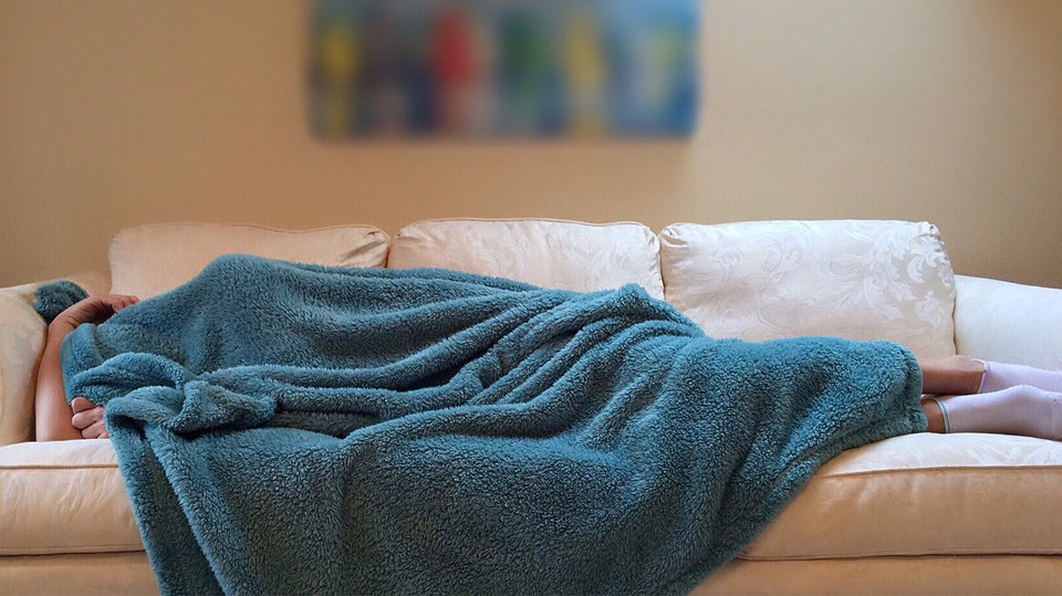 Imagen de un joven tratando de dormir en un sofá, cubierto con una manta ARCHIVO