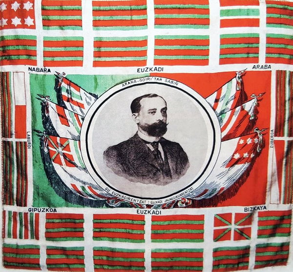 La ikurriña inventada por Sabina Arana Goiri y representada en un pañuelo diseñado por Luis Arana, con la efigie de Sabino Arana.