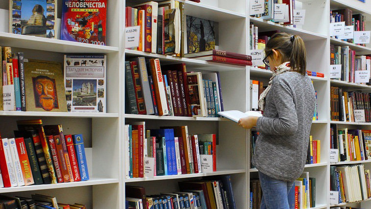 Una mujer en una biblioteca leyendo un libro.