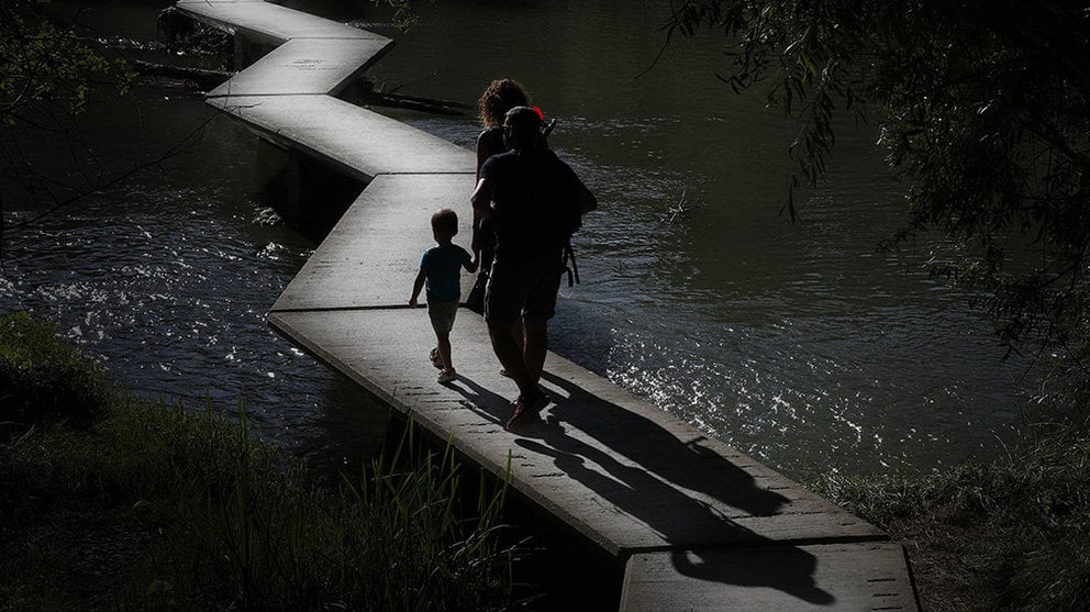 Una familia atraviesa la pasarela del río Arga a su paso por Pamplona en un día marcado por el tiempo soleado y el calor veraniego. EFE/Villar López