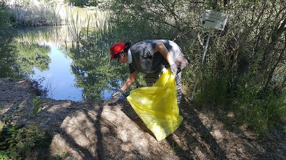 Una persona se agacha a recoger basura a la orilla de un río PROYECTO LIBERA