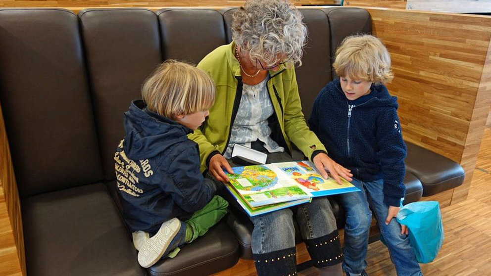 Una mujer lee un libro acompaña de dos niños ARCHIVO