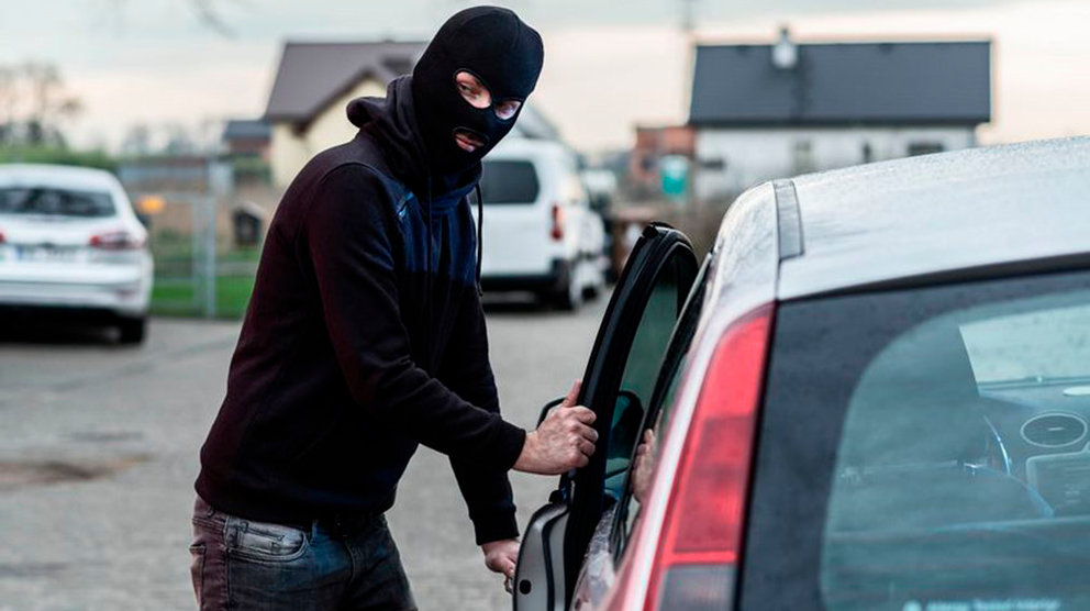 Un ladrón encapuchado fuerza la puerta del conductor de un coche para robarlo ARCHIVO