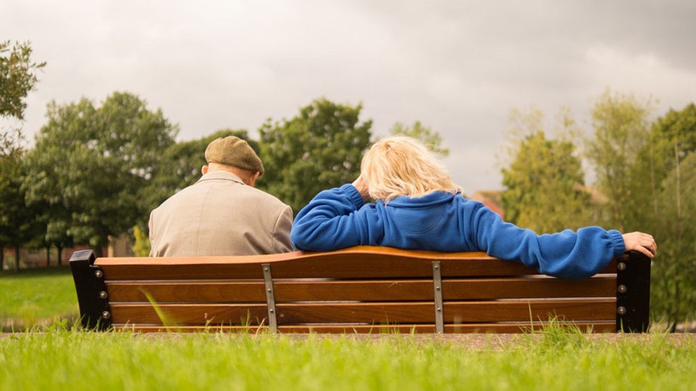 Imagen de una persona mayor sentada en un banco en un parque junto a una joven ARCHIVO