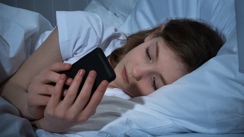 Imagen de una niña realizando una llamada desde su teléfono en la cama de su dormitorio ARCHIVO