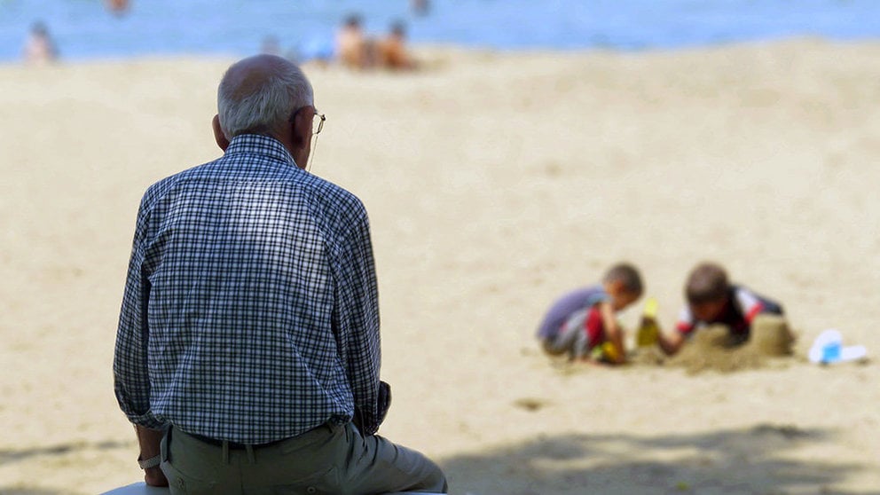Un hombre mayo observa a unos niños jugar en la arena.
