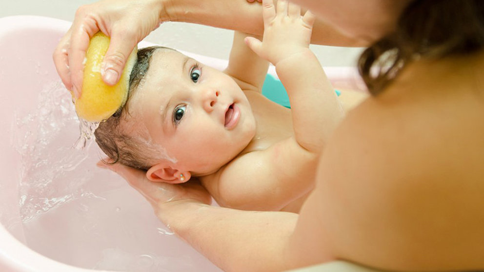 Una madre baña a su bebé en una bañera y le frota la cabeza con una esponja ARCHIVO