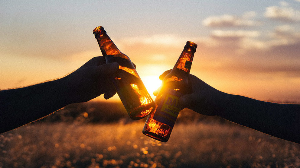 Dos personas brindan con unas cervezas bajo una puesta de sol.