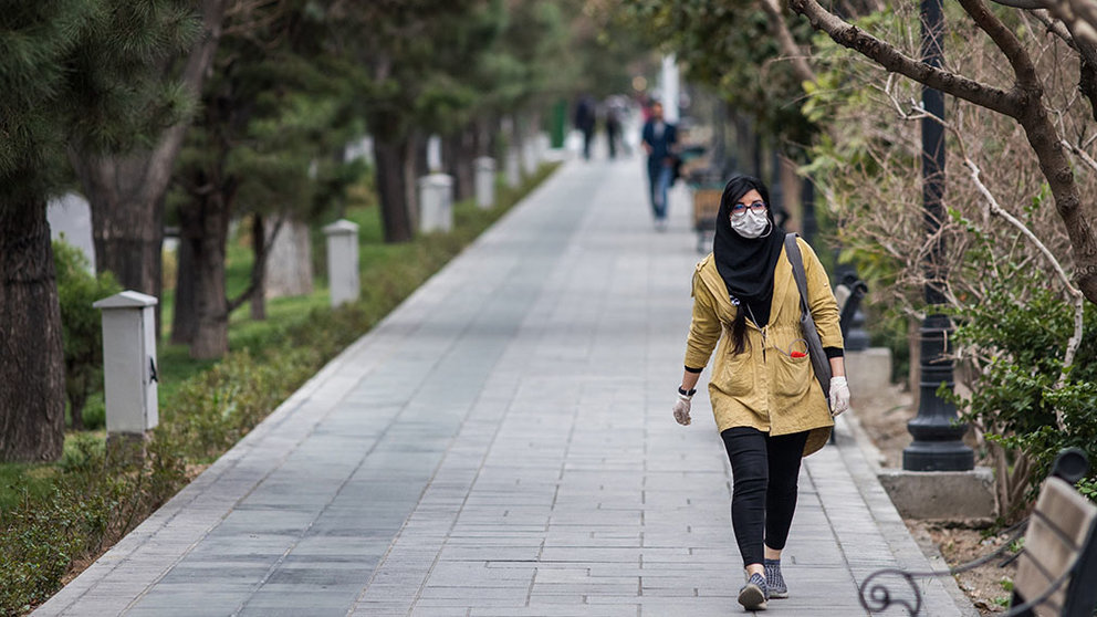 Una mujer pasea por un parque con mascarilla. Arash Khamooshi