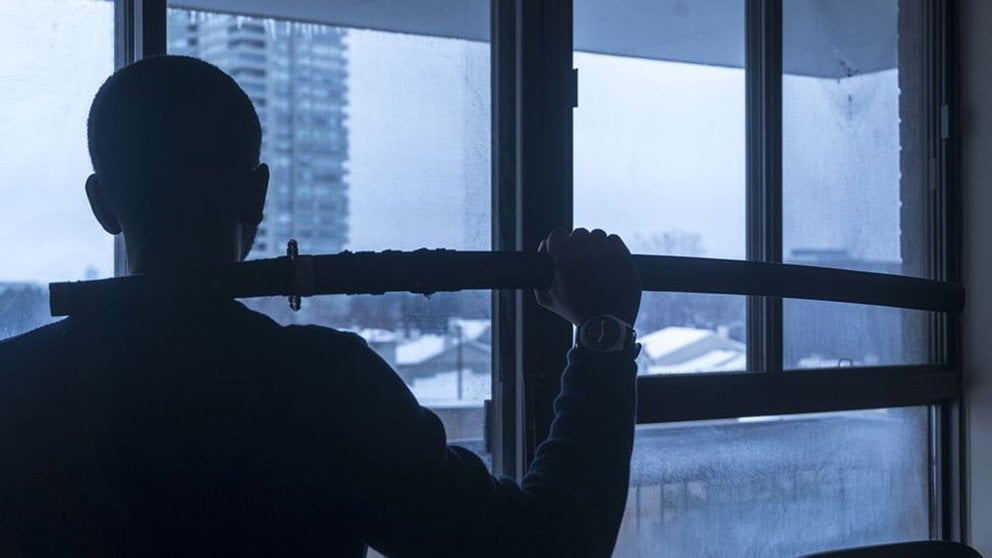 Un hombre mira por la ventana mientras sujeta una katana en la mano ARCHIVO
