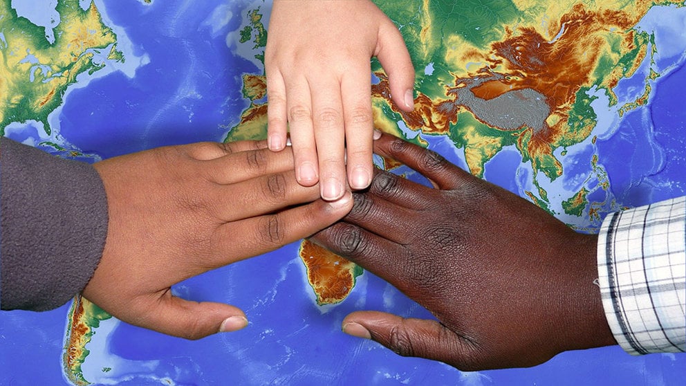 Tres niños migrantes unen sus manos sobre un mapamundi. ARCHIVO