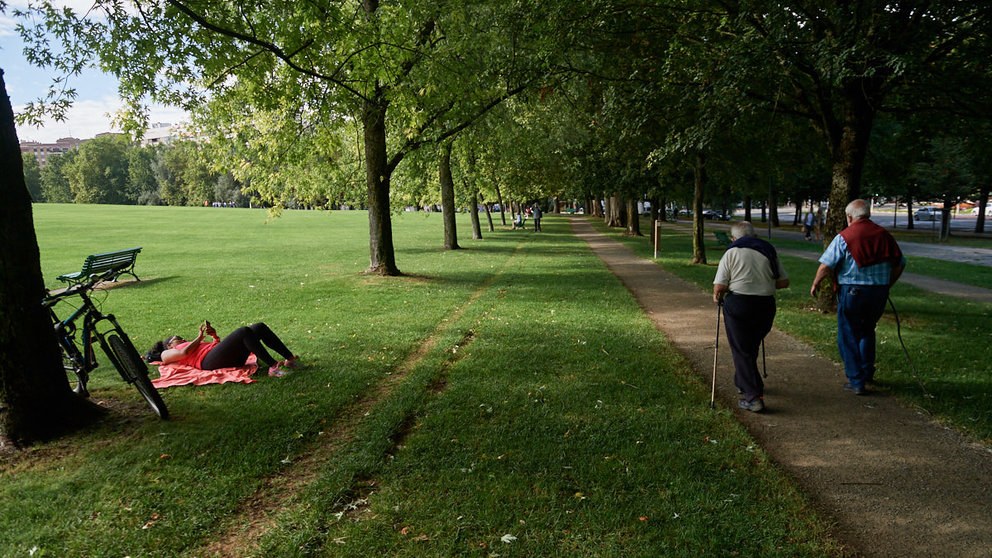 Dos señores caminan por la vuelta del castillo de Pamplona mientras una mujer descansa tumbada sobre la hierba, en los últimos dias de verano de 2021- MIGUEL OSÉS