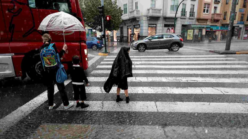 Una madre con sus dos hijos aguarda a cruzar por un paso de peatones durante una tormenta en Pamplona.  EFE/ Jesús Diges