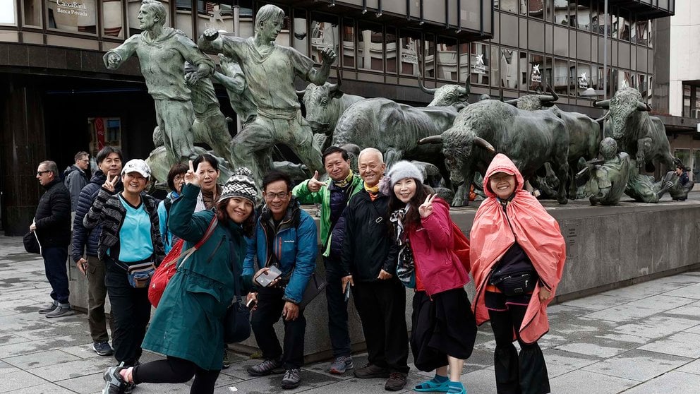 En una jornada muy desapacible en la capital navarra con el descenso de temperaturas y lluvia intermitente un grupo de turistas de Taiwan se toman una fotografía con el monumento al encierro que se encuentra en el centro de Pamplona.  EFE/ Jesús Diges