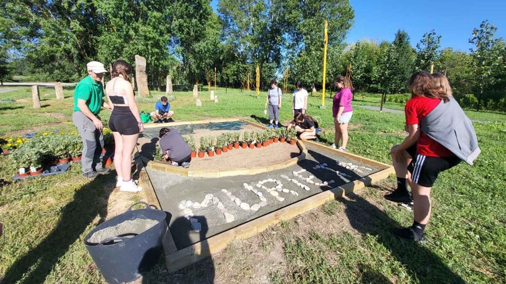 Un grupo de chicas y un jardinero crean el escudo de Murieta con plantas, flores y piedras. Cedida.