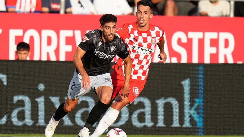 El delantero macedonio del Girona Bojan Miovski (d) disputa un balón ante el defensa Nacho Vidal del Osasuna este jueves, durante el partido de la jornada 3 de LaLiga EA Sports, entre el Girona FC y el CA Osasuna, en el estadio Montilivi de Girona. EFE/ Siu Wu