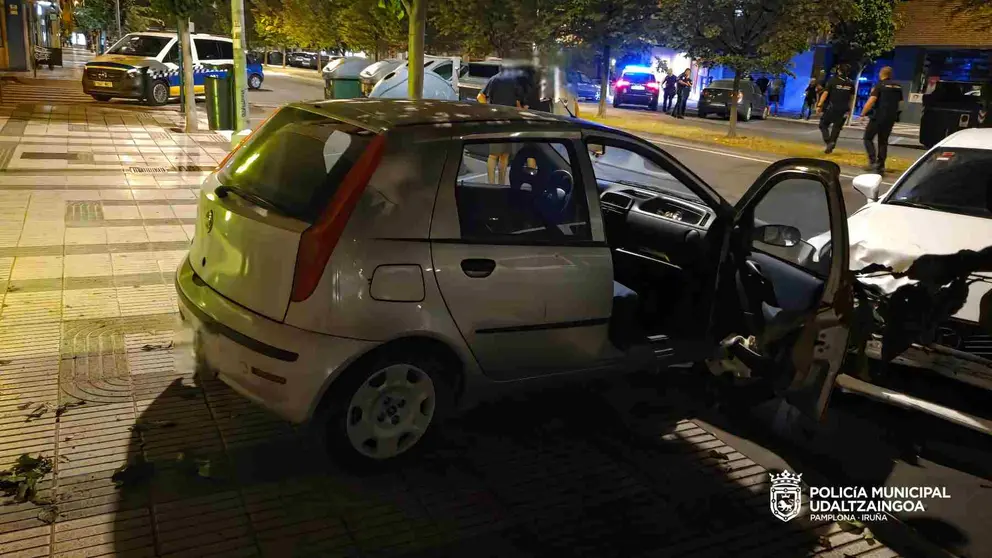 El coche se subió a la acera rompió dos vallas de protección y se estampó contra otro coche que estaba aparcado. POLICÍA MUNICIPAL DE PAMPLONA
