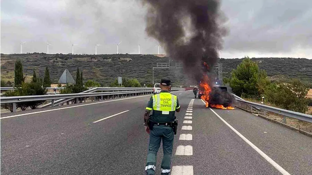 Un agente de la Guardia Civil ante el vehículo ardiendo en la subida al Perdón por la A-12, en Legarda. GUARDIA CIVIL