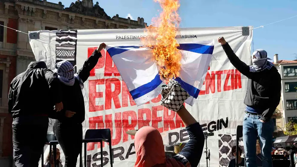 Varios encapuchados queman una bandera israelí durante una marcha que ha recorrido las calles del centro de Pamplona en solidaridad con el pueblo palestino. EFE/ Jesús Diges