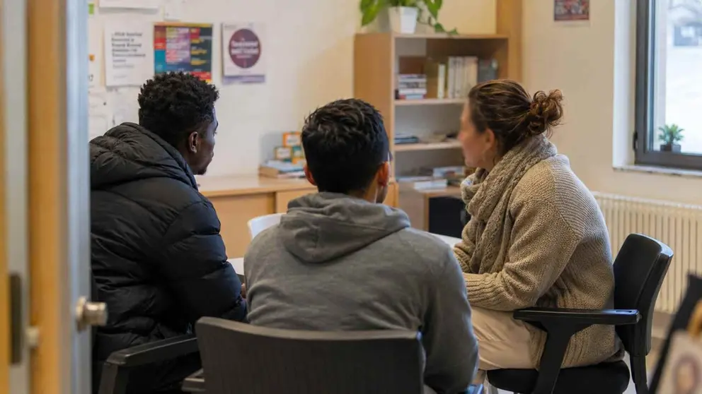 Imagen generada con inteligencia artificial de una educadora social manteniendo una conversaci&oacute;n con dos inmigrantes. CHAT GPT
