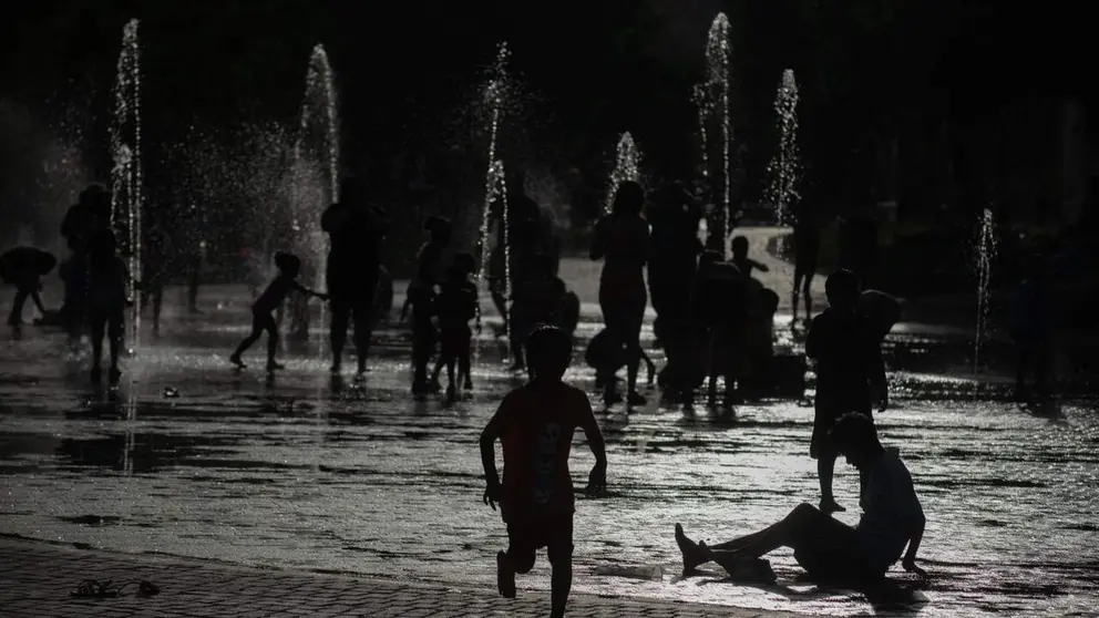 Varias personas se refrescan en una fuente.