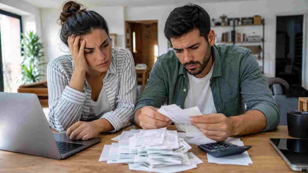 Una pareja en el sal&oacute;n de su casa mirando con preocupaci&oacute;n facturas y tickets de compra.