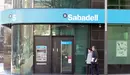 Dos personas pasan por delante de una oficina del Banco Sabadell.