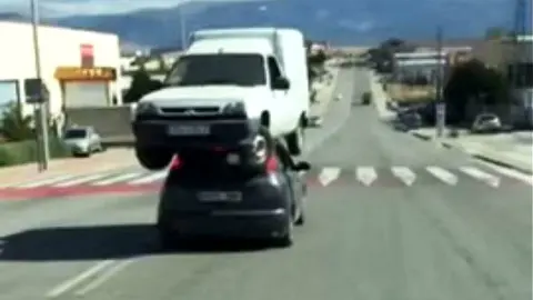 Un conductor lleva sobre el techo de su coche una furgoneta averiada.
